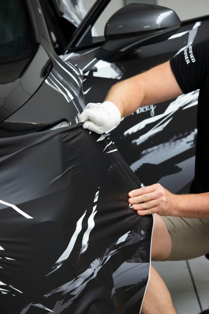 Man working in a garage, applying a vinyl wrap to a vehicle for customization.