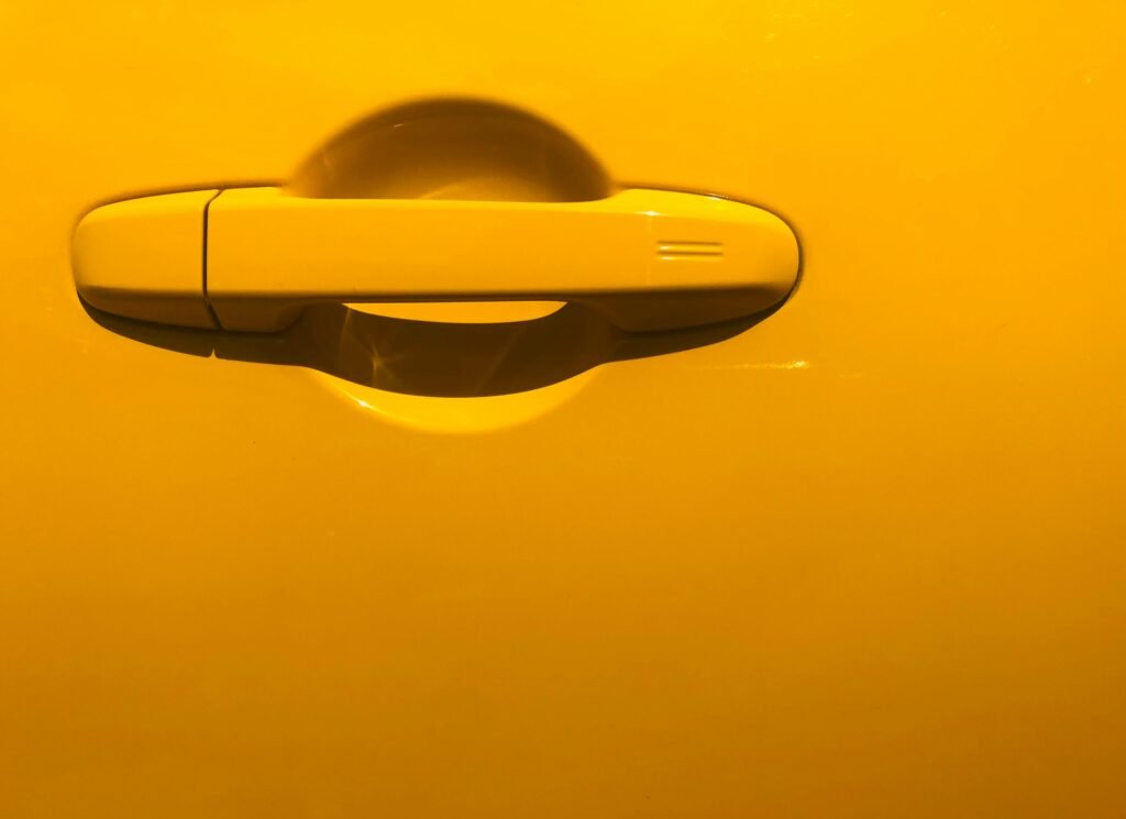 Close-up of a bright yellow car door handle with dramatic lighting and reflections.